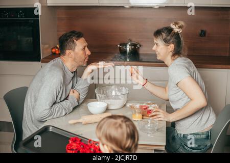 Junge Familie haben Spaß beim Reden in der Küche, mitgenommen vom Backen von Cookies. Papa und Mama. Arbeiten Sie als Team zusammen, Sohn trägt Backblech mit Cookie Stockfoto