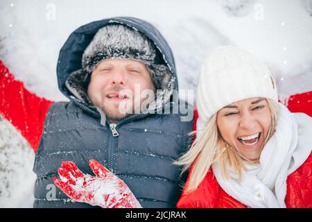 Winter, mittleres Alter Paar verliebt. Frau und Mann liegen umarmt und lachen auf weißem Schnee. Romantisches Paar haben Winterspaß, Liebesgeschichte im Freien Stockfoto