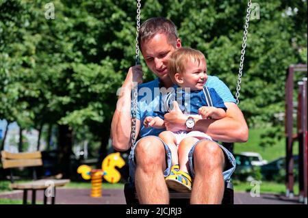 Vater schwingt mit seinem kleinen Jungen auf dem Spielplatz Stockfoto