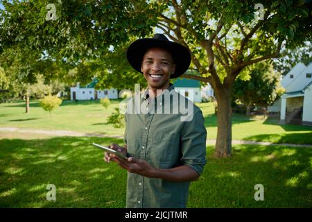 Gemischter männlicher Landwirt, der im Freien steht und ein digitales Tablet hält Stockfoto
