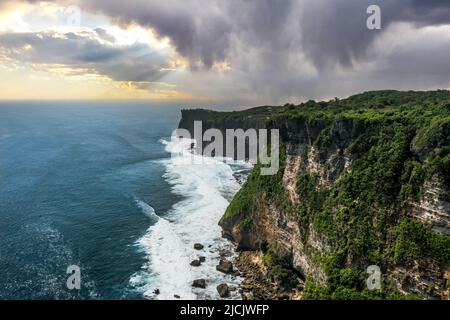 Höhenflug von großen Klippen in der Nähe des Nyang Nyang Strandes in Uluwatu Bali Indonesien an einem Sonnenuntergangsnachmittag mit Gewittern und Regen über dem Blau Stockfoto