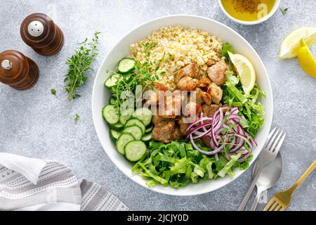 Salatschüssel mit Schweinebab-Bulgur, Gurke, Salat, Thymian und Senfsauce Stockfoto