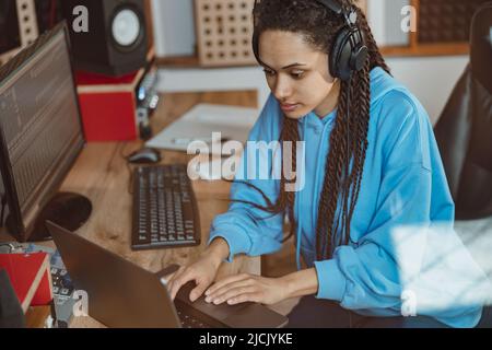 Afrikanerin, Radiomoderatorin, Toningenieurin in Kopfhörern, die Text auf dem Laptop tippt, während sie im Rundfunkstudio arbeitet Stockfoto