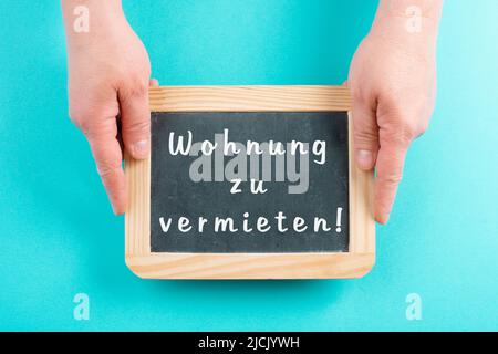 Mit einer Tafel in den Händen steht die Mietwohnung in deutscher Sprache auf dem Schild und zieht in ein neues Zuhause, eine Immobilie Stockfoto