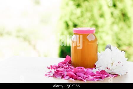 Glas mit Honig, rosa und weißen Blütenblättern und Pfingstrosen, isolieren Stockfoto