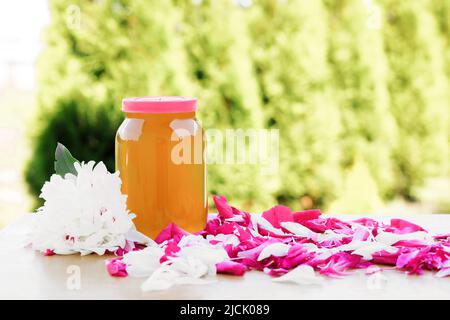 Frischer Honig mit Blumen und Pfingstrosen auf einem Holztisch Stockfoto