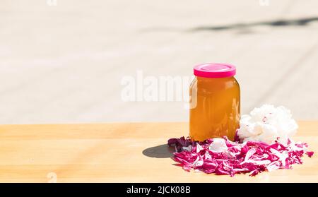 Frischer Honig mit Blumen und Pfingstrosen auf einem Holztisch Stockfoto