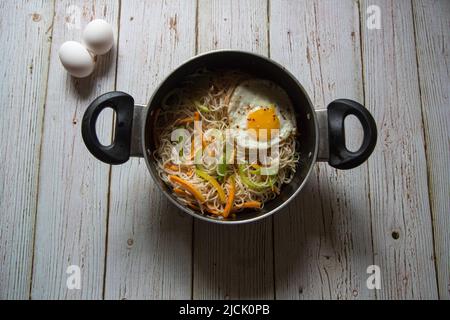 Gebratene Nudeln in einer Pfanne auf einem Hintergrund anbraten. Nahaufnahme, selektiver Fokus. Stockfoto