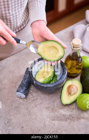 Nahaufnahme der Hände, die frische Avocado in zwei Hälften schneiden und Guacamole bilden Stockfoto