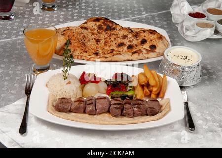 Shish Kebab wird aus Lamm hergestellt. Auf dem Esstisch stehen Shish Kebab, Pita-Brot und Fruchtsaft. Stockfoto