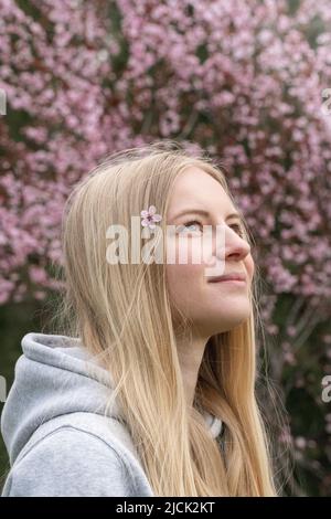 Porträt einer jungen blonden Frau mit rosa Kirschblüten im Haar Stockfoto