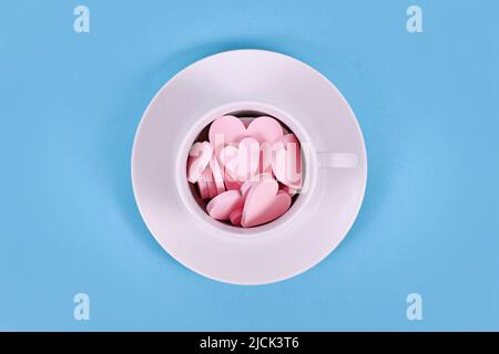 Pinkfarbene Herz-Ornamente aus Holz in weißer Teetasse auf blauem Hintergrund Stockfoto