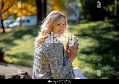 Schöne blonde Frau in leichter Tweed Jacke lächelt über ihre Schulter auf die Kamera schauen. Herbsttag in der Natur. Glück und Frieden. Frische Spaziergänge Stockfoto