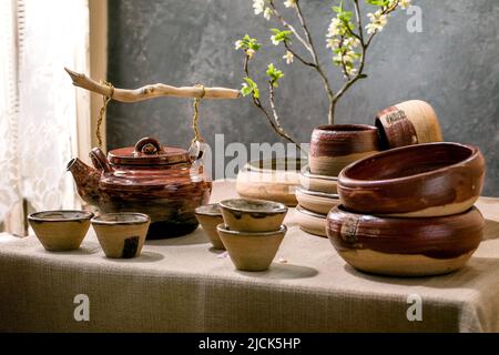 Japanische Tischdekoration im asiatischen Stil mit leerem Keramikgeschirr, braunen, rauen Schalen und Tassen auf Leinentischdecken, dekoriert von ikebana Spring Flo Stockfoto