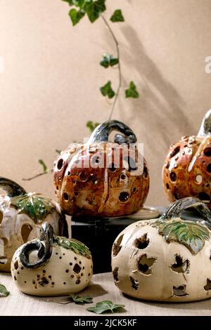 Halloween-Dekorationen, Set aus weißen und braunen handgefertigten geschnitzten Keramik-Kürbissen, die mit Efeu-Blättern auf dem Tisch stehen. Halloween oder Thanksgiving Stockfoto