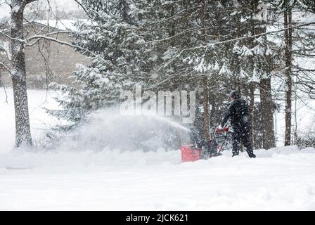 Mann, der am Schneetag die Auffahrt mit einer Schneefräse räumen muss. Stockfoto