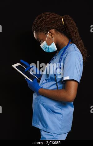 Schwarzer schwanger Arzt in Gesichtsmaske mit Tablet-Computer isoliert über dunklen Hintergrund Stockfoto