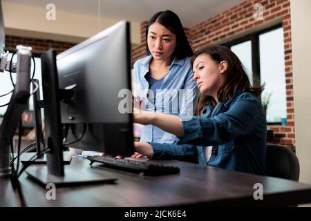 Professionelle Büroangestellte weisen auf falsche Projektvorlage hin, während sie einen Arbeitscomputer verwenden. Kreative Designer entwickeln digitale Kunst auf dem PC, während sie über 3D Technologie diskutieren. Stockfoto