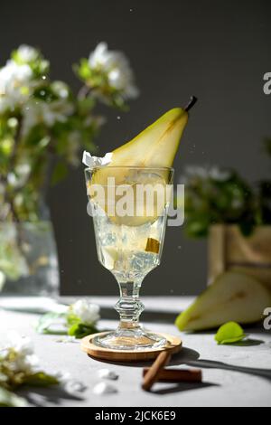 Birnencocktail mit Birnenpüree und frischem Obst und Blumen auf grauem Hintergrund und Schatten. Sommerlich kalte Birne Limonade mit Eis auf dem Tisch, Spark Stockfoto