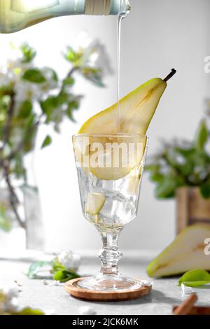 Birne Sirop ist in einem Glas mit Birne Cocktail mit frischem Obst und Blumen auf hellgrauem Hintergrund dekoriert gießen. Sommer kalt Birne trinken Limonade w Stockfoto