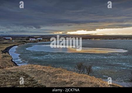 Blick über den See Myvatn in Island, teilweise gefroren unter dunklen Wolken mit einem Streifen klaren Himmels und Sonnenlicht am Horizont Stockfoto