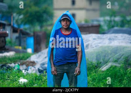 Bhaktapur, Bagmati, Nepal. 14.. Juni 2022. Ein Bauer bedeckt sich mit einer Plastikfolie, während er während eines Monsunregens in Bhaktapur, Nepal, auf einem Reisfeld arbeitet. (Bild: © Amit Machamasi/ZUMA Press Wire) Stockfoto