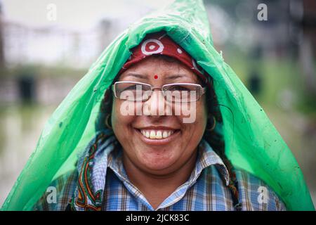 Bhaktapur, Bagmati, Nepal. 14.. Juni 2022. Eine Frau mit einem Plastiktuch, das ihren Kopf bedeckt, lächelt auf die Kamera, während sie am Montag in Bhaktapur Reisig auf ihr Feld pflanzt. (Bild: © Amit Machamasi/ZUMA Press Wire) Stockfoto