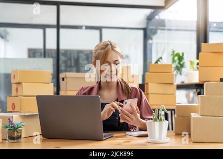 Startup Kleinunternehmen Unternehmer KMU freiberufliche Frau arbeiten mit Handy, Young Asian Besitzer verwenden Computer, Online-Markt Verpackung Box Lieferung Stockfoto