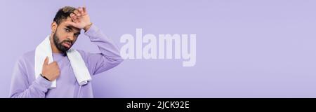 Müde afroamerikanische Mann in Pullover mit weißem Handtuch und wischen Schweiß mit Hand isoliert auf lila, Banner Stockfoto