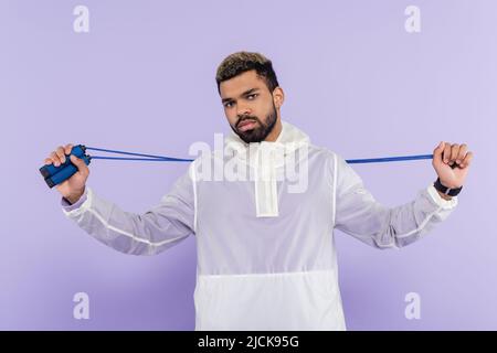 Bärtiger afroamerikanischer Sportler, der Springseil isoliert auf Purpur hält Stockfoto