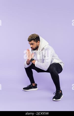 Die ganze Länge des bärtigen afroamerikanischen Sportlers in Sportkleidung, der mit betenden Händen auf Purpur ausarbeitet Stockfoto