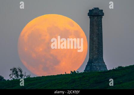 Portesham, Dorset, Großbritannien. 13.. Juni 2022. Wetter in Großbritannien. Der fast volle Strawberry Super Moon leuchtet orange, als er sich hinter dem Hardy Monument in Portesham in Dorset in den klaren Abendhimmel erhebt. Das Denkmal wurde 1844 in Erinnerung an den Vizeadmiral Sir Thomas Masterman Hardy errichtet, der Flaggenkapitän der HMS Victory bei der Schlacht von Trafalgar war. Bildnachweis: Graham Hunt/Alamy Live News Stockfoto