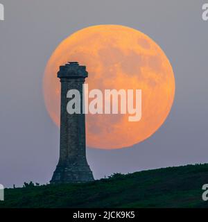 Portesham, Dorset, Großbritannien. 13.. Juni 2022. Wetter in Großbritannien. Der fast volle Strawberry Super Moon leuchtet orange, als er sich hinter dem Hardy Monument in Portesham in Dorset in den klaren Abendhimmel erhebt. Das Denkmal wurde 1844 in Erinnerung an den Vizeadmiral Sir Thomas Masterman Hardy errichtet, der Flaggenkapitän der HMS Victory bei der Schlacht von Trafalgar war. Bildnachweis: Graham Hunt/Alamy Live News Stockfoto