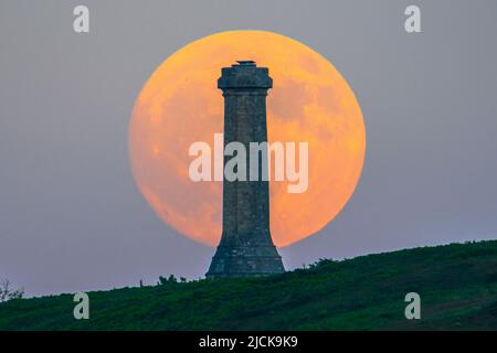 Portesham, Dorset, Großbritannien. 13.. Juni 2022. Wetter in Großbritannien. Der fast volle Strawberry Super Moon leuchtet orange, als er sich hinter dem Hardy Monument in Portesham in Dorset in den klaren Abendhimmel erhebt. Das Denkmal wurde 1844 in Erinnerung an den Vizeadmiral Sir Thomas Masterman Hardy errichtet, der Flaggenkapitän der HMS Victory bei der Schlacht von Trafalgar war. Bildnachweis: Graham Hunt/Alamy Live News Stockfoto
