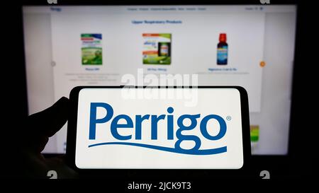 Person, die das Smartphone mit dem Logo des Pharmaherstellers Perrigo Company plc auf dem Bildschirm vor der Website hält. Konzentrieren Sie sich auf die Telefonanzeige. Stockfoto