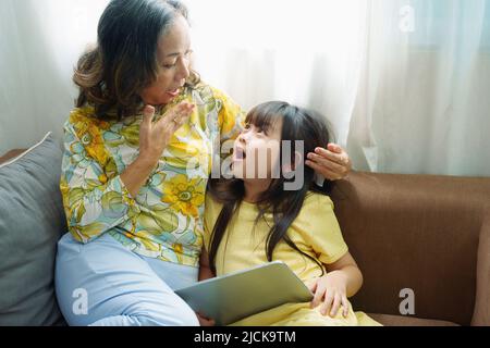 Asiatisches Porträt, Oma und Enkelin machen Freizeitaktivitäten und spielen Tablet-Computer auf dem Sofa Stockfoto