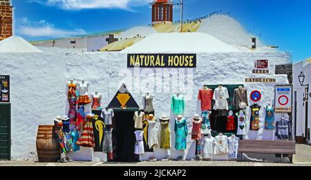 Teguise, Lanzarote - Juin 3. 2019: Schöne weiße ruhige kanarische Stadt, traditionelles Bekleidungsgeschäft, kleine schmale Gasse, Kirchturm, blauer Himmel (Fokus Stockfoto