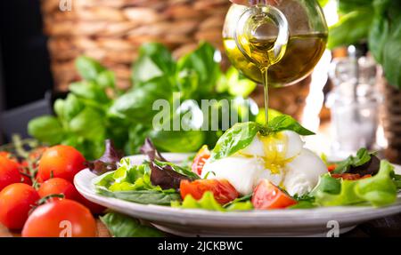 Salat mit Tomaten, Burrata, Basilikum, Olivenöl. Zweiter Vorname Burratina. Traditioneller Käse aus Süditalien in der Region Apulien. Runder weicher Käse in flüssiger Stracciatella-Textur Stockfoto