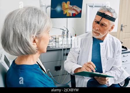 Grauhaariger Arzt, der im HNO-Zentrum eine Konsultation für eine ältere Patientin mit gesundheitlichen Problemen macht. Konsultation des HNO-Arztes Stockfoto