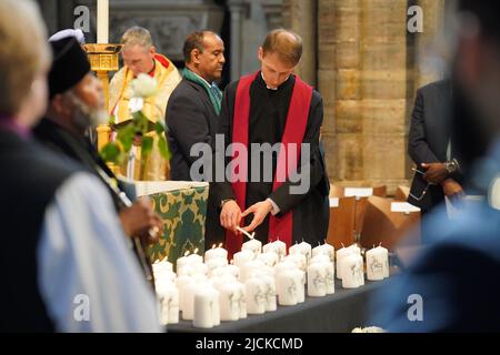 Ein Mitglied des Klerus zündet während des Grenfell-Feuergedenkens in der Westminster Abbey in London Kerzen mit den Namen der Opfer an, um an diejenigen zu erinnern, die am 14 2018. Juni beim Feuer im Grenfell Tower ums Leben kamen. Bilddatum: Dienstag, 14. Juni 2022. Stockfoto