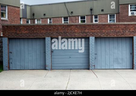 STADTLANDSCHAFT. Drei Garagentore in Cyanblau mit zweistöckigen Apartments im Hintergrund. Auf dem Francis Lewis Boulevard in Queens, New York. Stockfoto