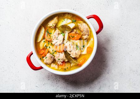 Hühnereintopf mit Kartoffeln und Karotten im roten Topf, Draufsicht, Kopierraum. Hühnersuppe mit Gemüse und Kräutern. Rezept für ein bequemes Essen. Stockfoto