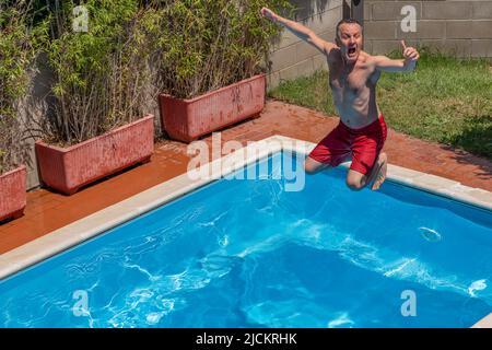 Blick von oben auf einen kaukasischen Mann, der an einem sonnigen Tag einen lustigen Tauchgang im Pool macht Stockfoto