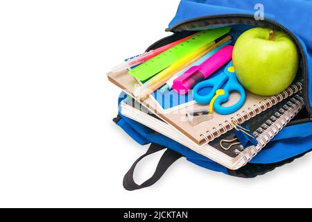 Die blaue Schultasche der Schüler ist gefüllt mit Notizbüchern, Stiften, Markern, Papeterie und einem grünen Apfel liegt auf seiner Seite, isoliert auf weißem Hintergrund. Stockfoto