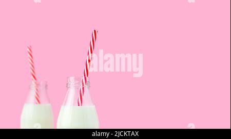 Frische Milch in einer Glasflasche, Haferflocken, Mandel, alternative natürliche Getränk. Zwei Flaschen gesundes Bio-Getränk mit gestreiften Trinkhalmen auf einem rosa. Stockfoto