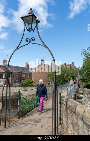 Menschen, die auf einer Fußgängerbrücke über den Fluss Wansbeck in Morpeth, Northumberland, Großbritannien, spazieren gehen. Stockfoto