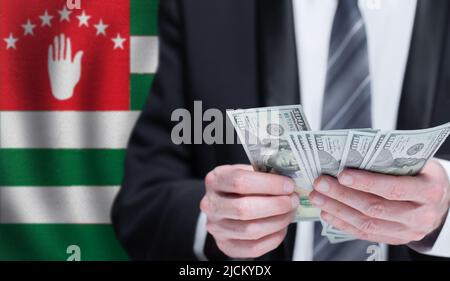 Hände, die Dollargeld auf der Flagge Abchasiens halten Stockfoto