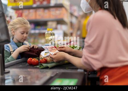 Nahaufnahme eines kleinen blonden Mädchens, das für den Einkauf im Supermarkt bezahlt. Stockfoto