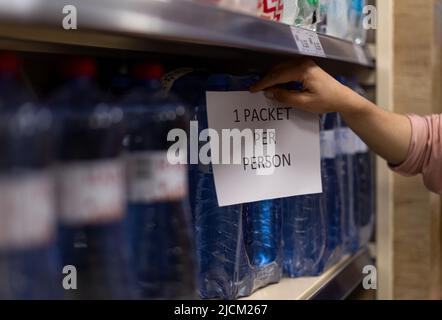 Die Frau nimmt Mineralwasser aus Superaket-Regalen, der Verkauf ist während der Krise auf ein Päckchen pro Person begrenzt. Stockfoto