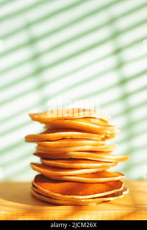 Stapel von leckeren Pfannkuchen auf Holzplatte und Schatten Hintergrund. Weicher, selektiver Fokus. Hausmannskost-Konzept. Stockfoto